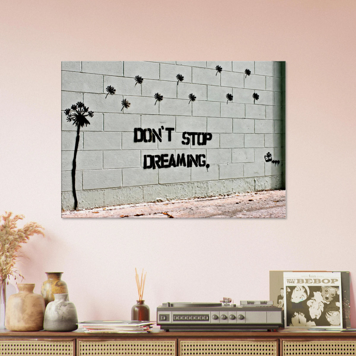 Don't Stop Dreaming Banksy street art canvas above a retro cabinet on a pale pink wall.